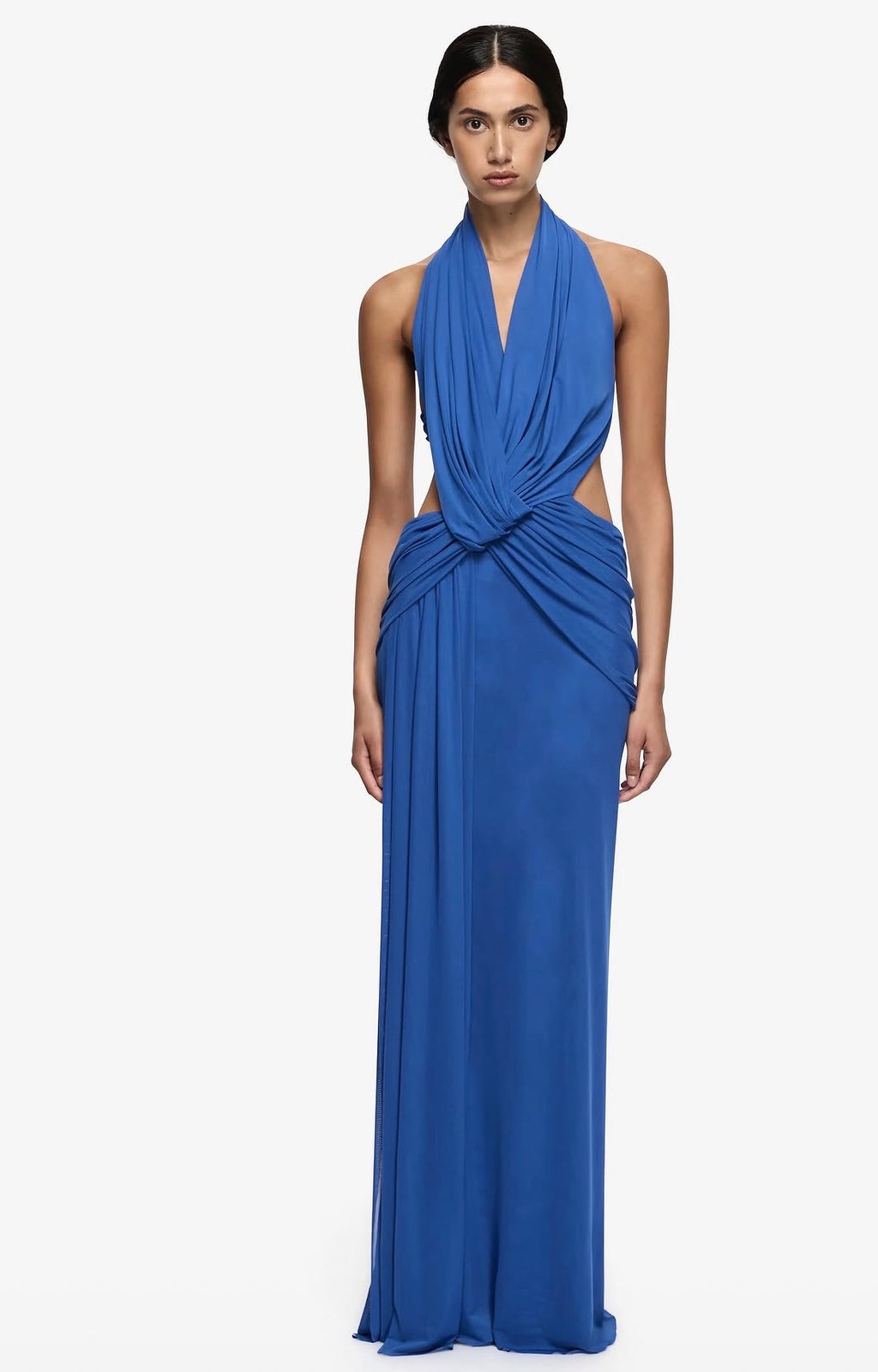 A model wearing a royal blue halter-neck maxi dress with a twisted draped waist and side cutouts, photographed against a plain white studio background.