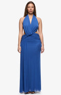 A woman modeling a royal blue halter-neck maxi dress with a twisted waist detail and side cutouts, set against a plain light gray studio background.