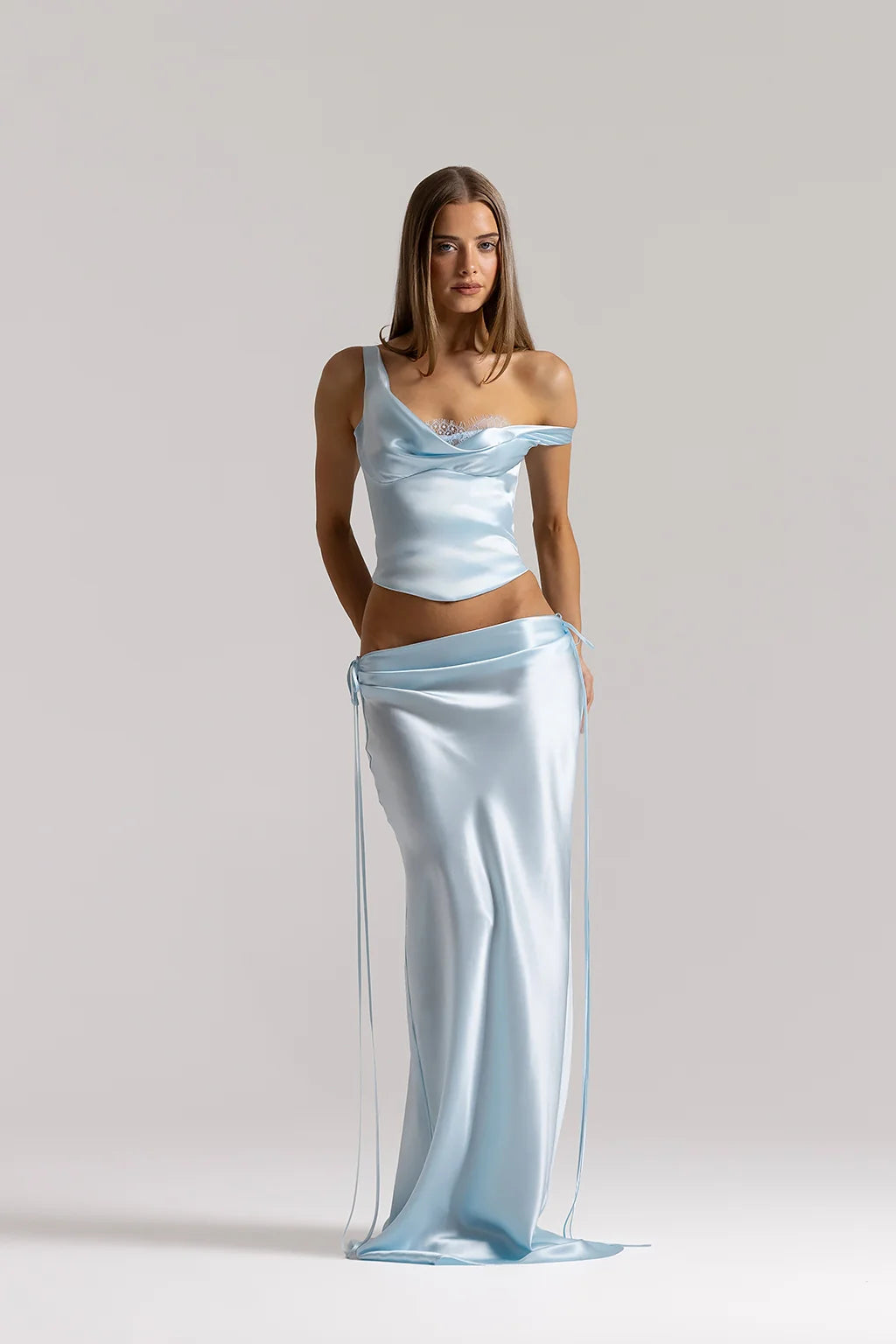Model wearing the Natalie Rolt Evelyn Skirt in Ice Blue, a full-length bias-cut silk skirt featuring draped waist detailing and elongated side ties, styled with the matching Posy Top.
