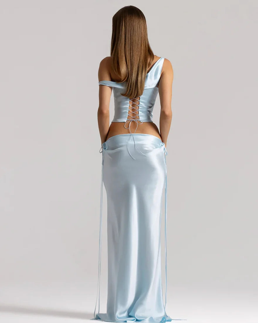 Rear view of a model wearing the Natalie Rolt Evelyn Skirt in Ice Blue, featuring a full-length bias-cut silk silhouette with draped waist detailing and elongated side ties, styled with the matching Posy Top.
