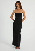 A woman modeling a strapless black maxi dress with a textured, ruched bodice and a fitted silhouette, standing against a plain light gray studio background.