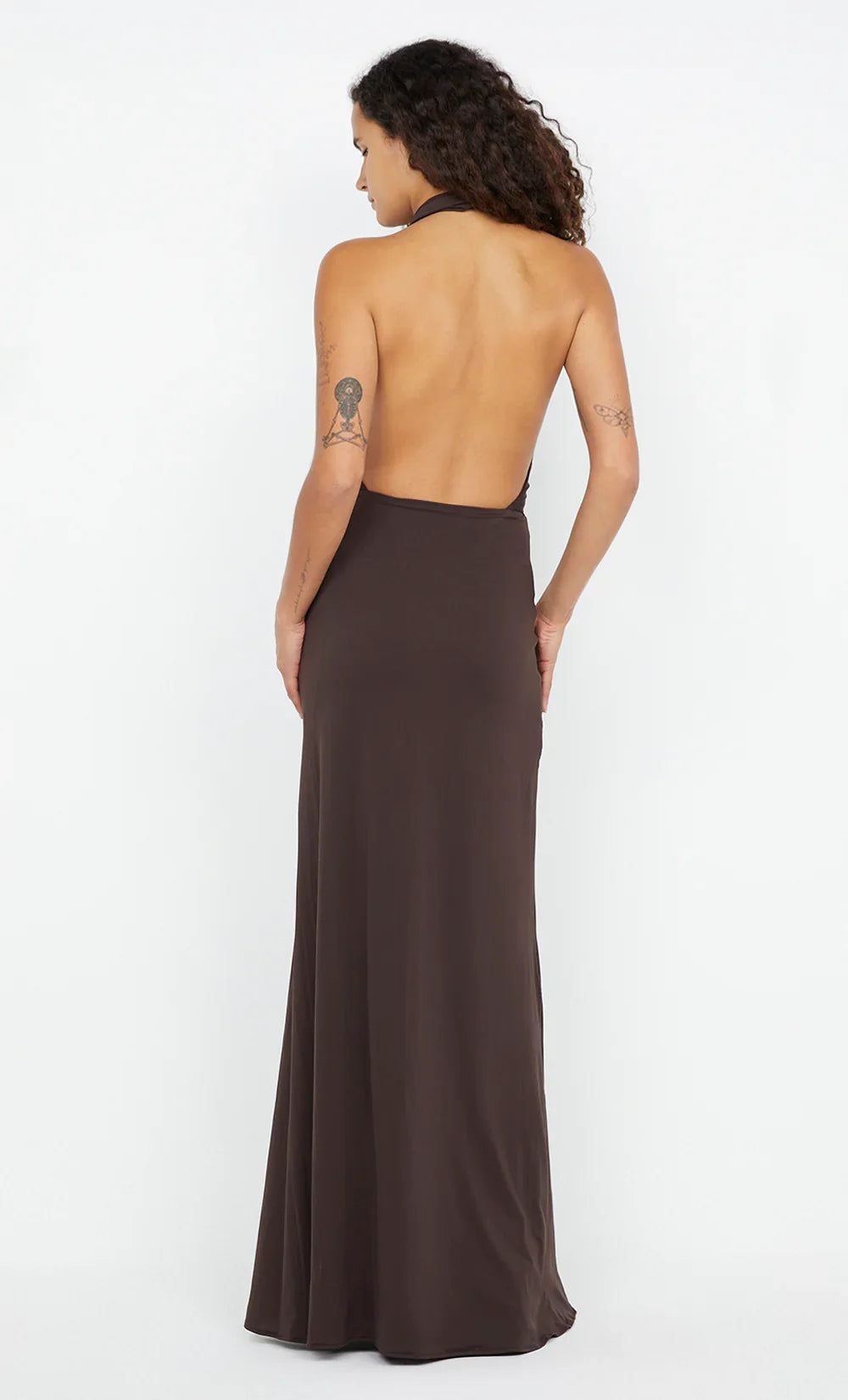A woman shown from the back wearing a dark brown, strapless halter-neck maxi dress with a fitted silhouette and a draped open back, set against a plain white studio background.