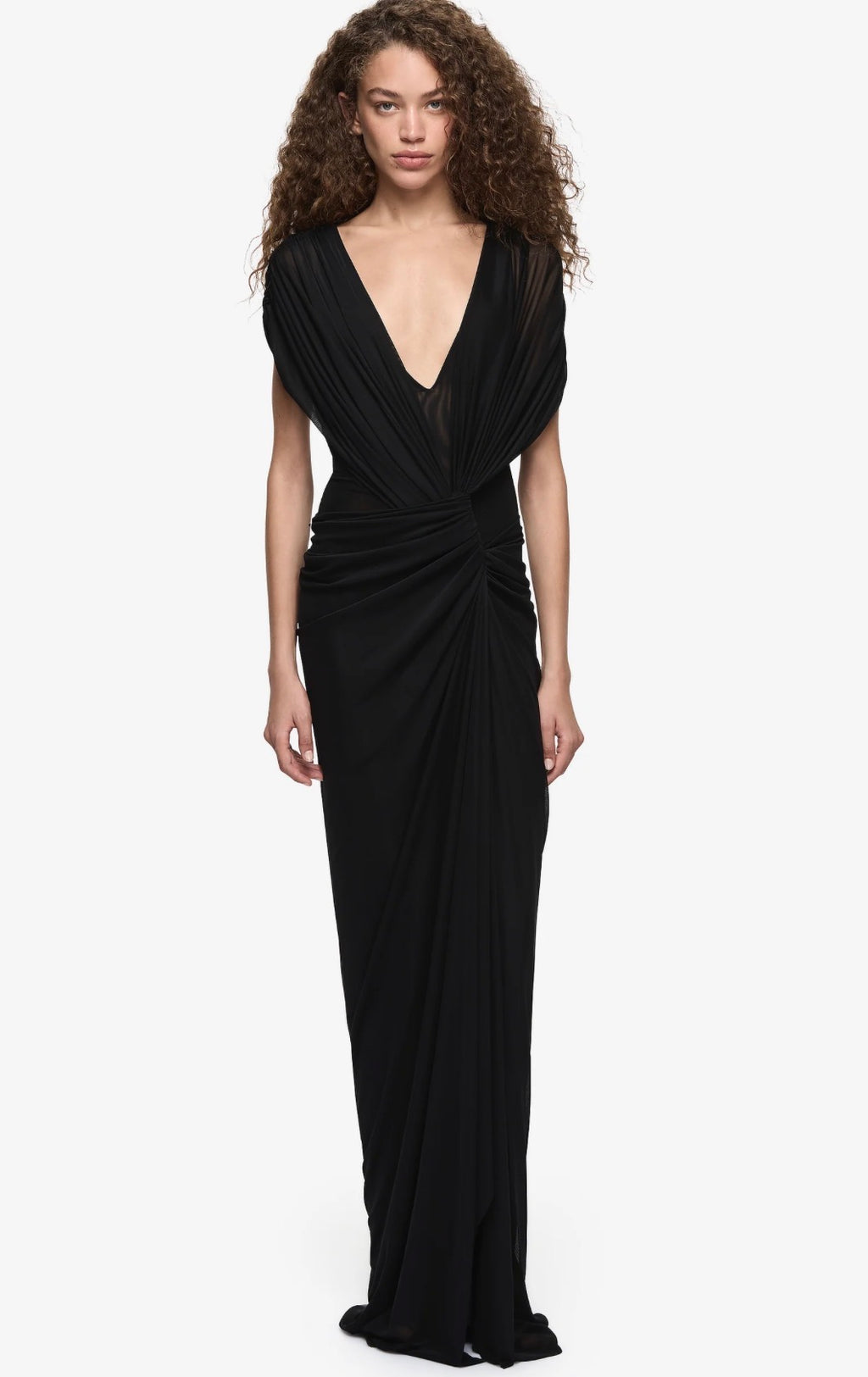  Model wearing a black draped mesh maxi dress with a deep V neckline, gathered twist detailing at the waist and a flowing floor-length silhouette.
