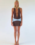 Model wearing the Sola Musa Oma Mini Dress in Bruna, featuring a deep V brown halter neckline, open silhouette and contrasting sky blue curved drop-waist panel.
