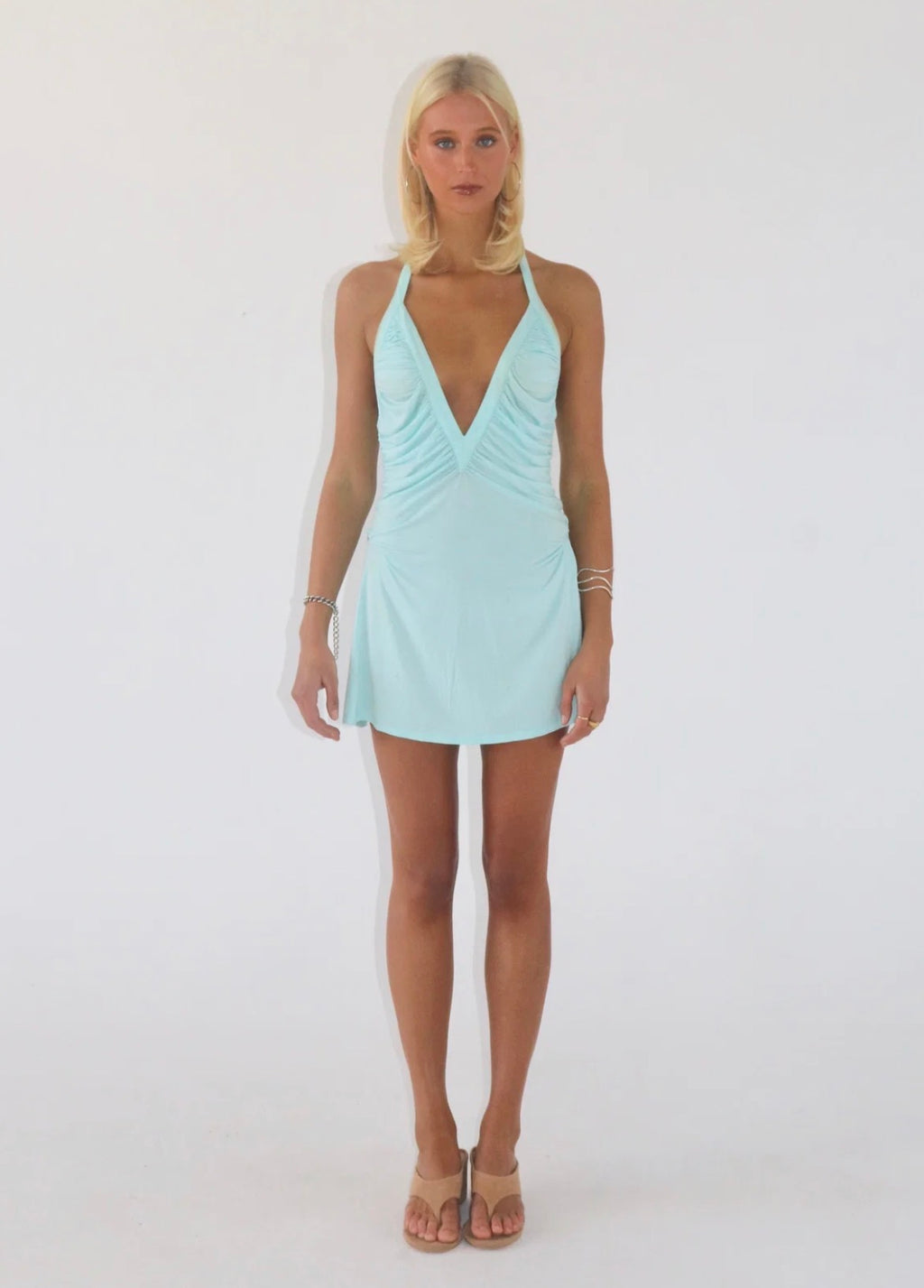 Model wearing the Angelina Mini Dress in light blue, featuring a deep V halter neckline, ruched bodice and flattering fitted mini silhouette.
