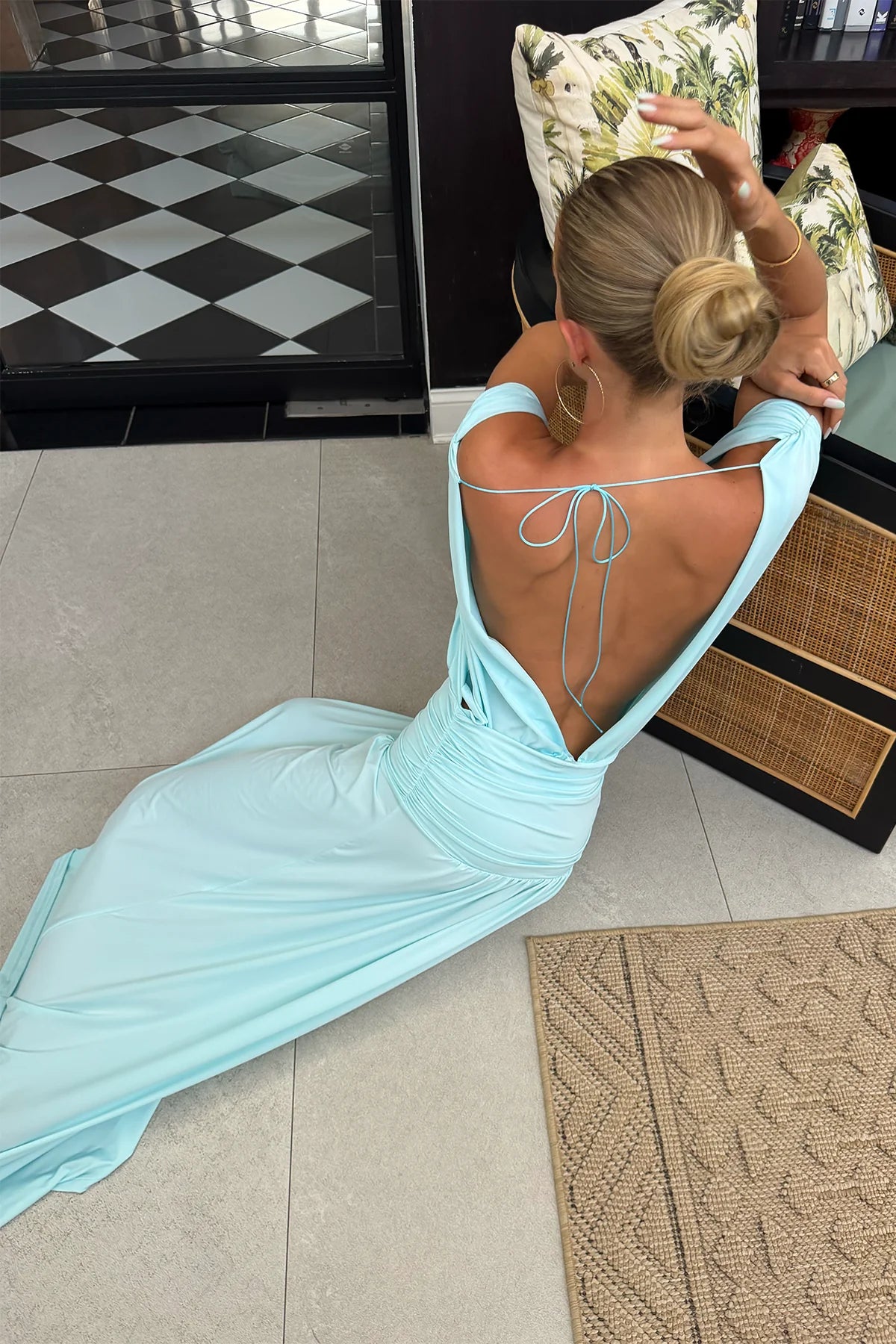 A women facing her back towards the camera wearing a blue maxi dress with a tie up back