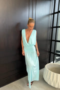 model wearing a long aqua maxi dress in front of a dark brown wall