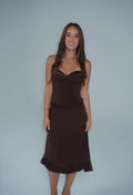 Woman wearing a chocolate brown fitted bustier-style top with a matching satin-trimmed midi skirt, standing against a light grey studio background. - @sarahmadden