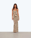 A woman modeling a sleeveless maxi dress with a beige and brown animal print pattern, standing against a plain light gray studio background.