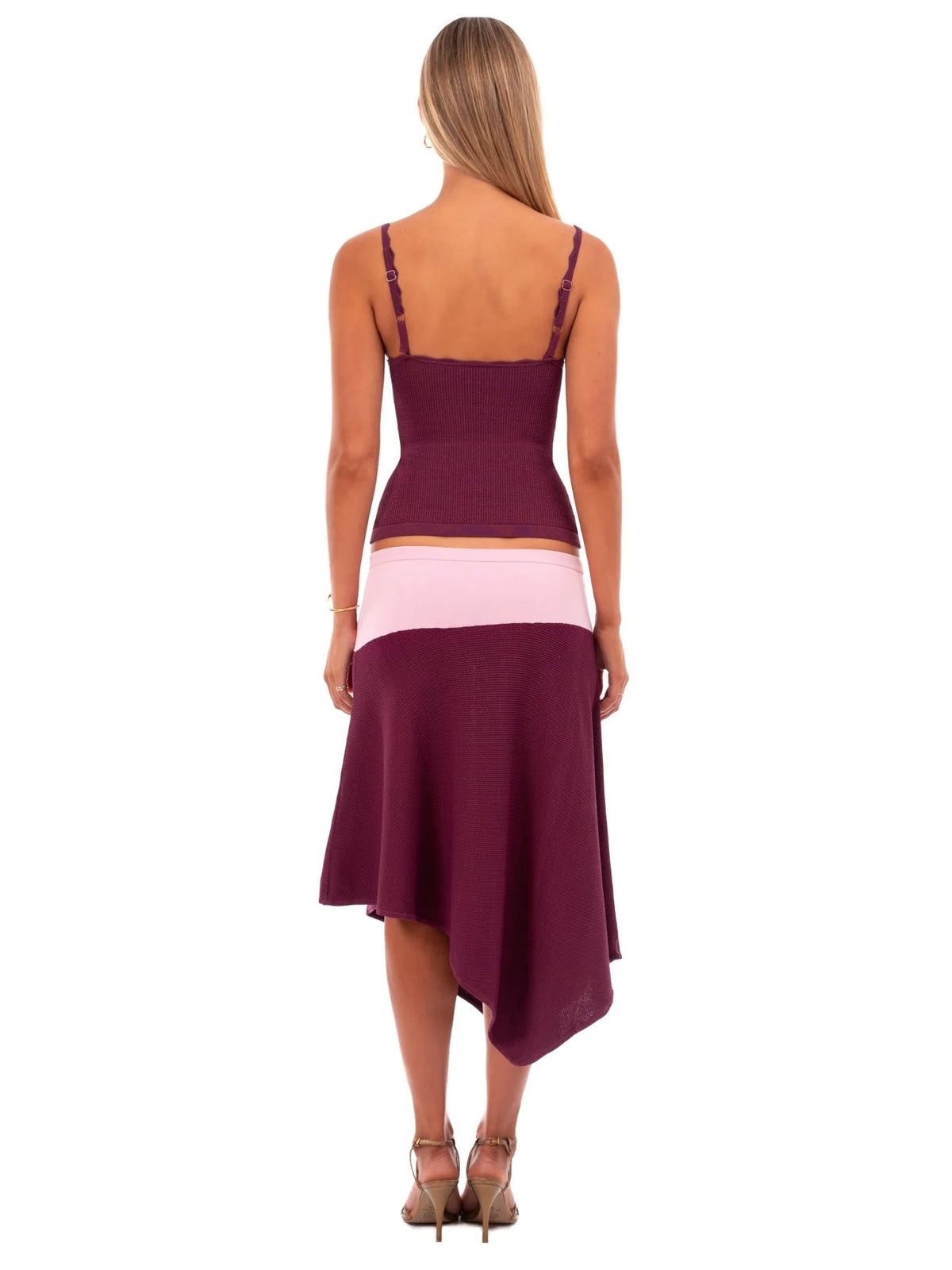 A woman shown from the back wearing a sleeveless high-low dress with a deep V-neck, thin shoulder straps, a fitted waist, and a flowing skirt. The dress has a dark burgundy top section, a light pink waistband, and a darker burgundy skirt.