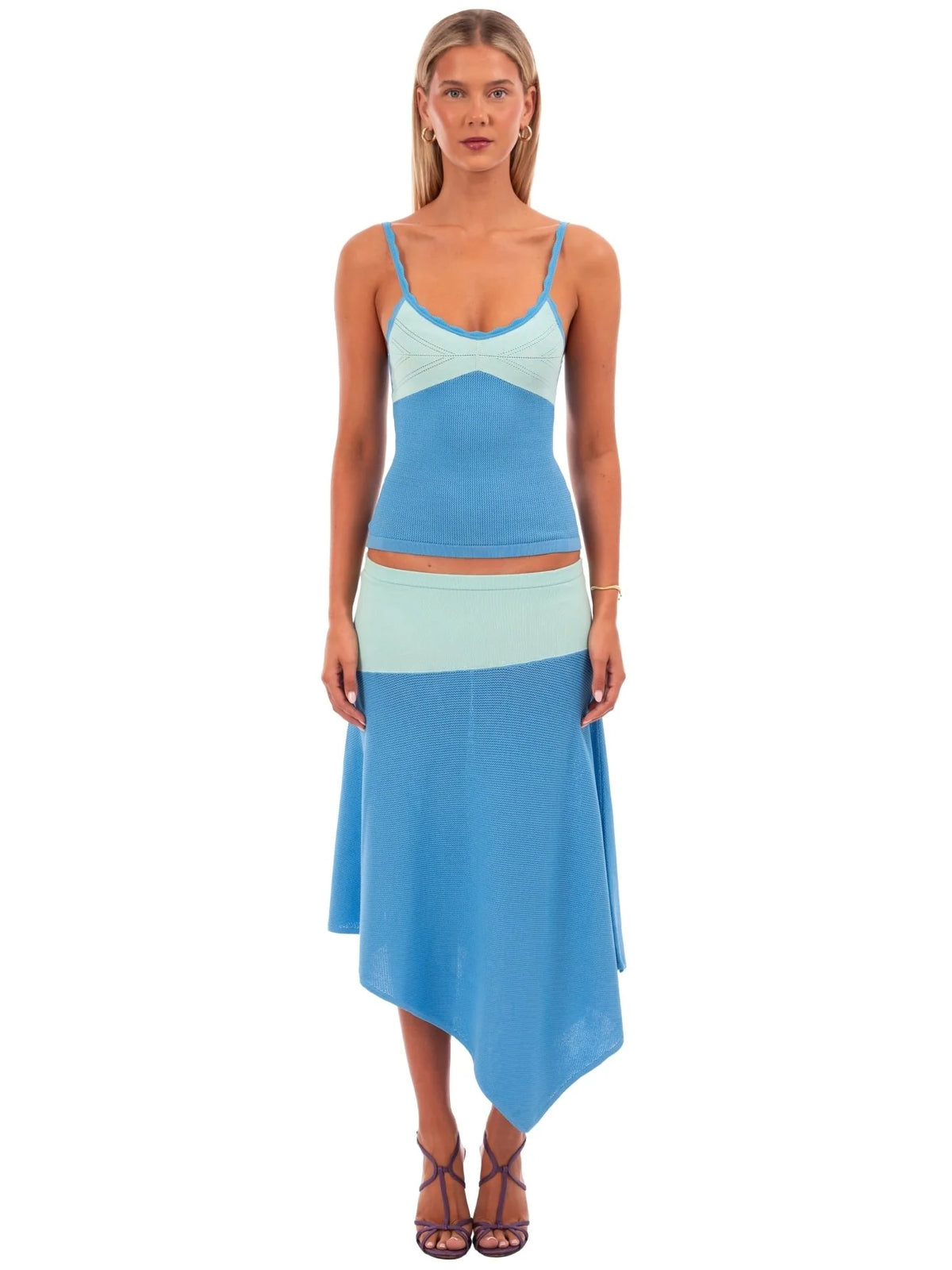 A woman modeling a two-piece color-blocked knit set featuring a light blue and mint green crop top with spaghetti straps and a matching high-low skirt, set against a plain white background.