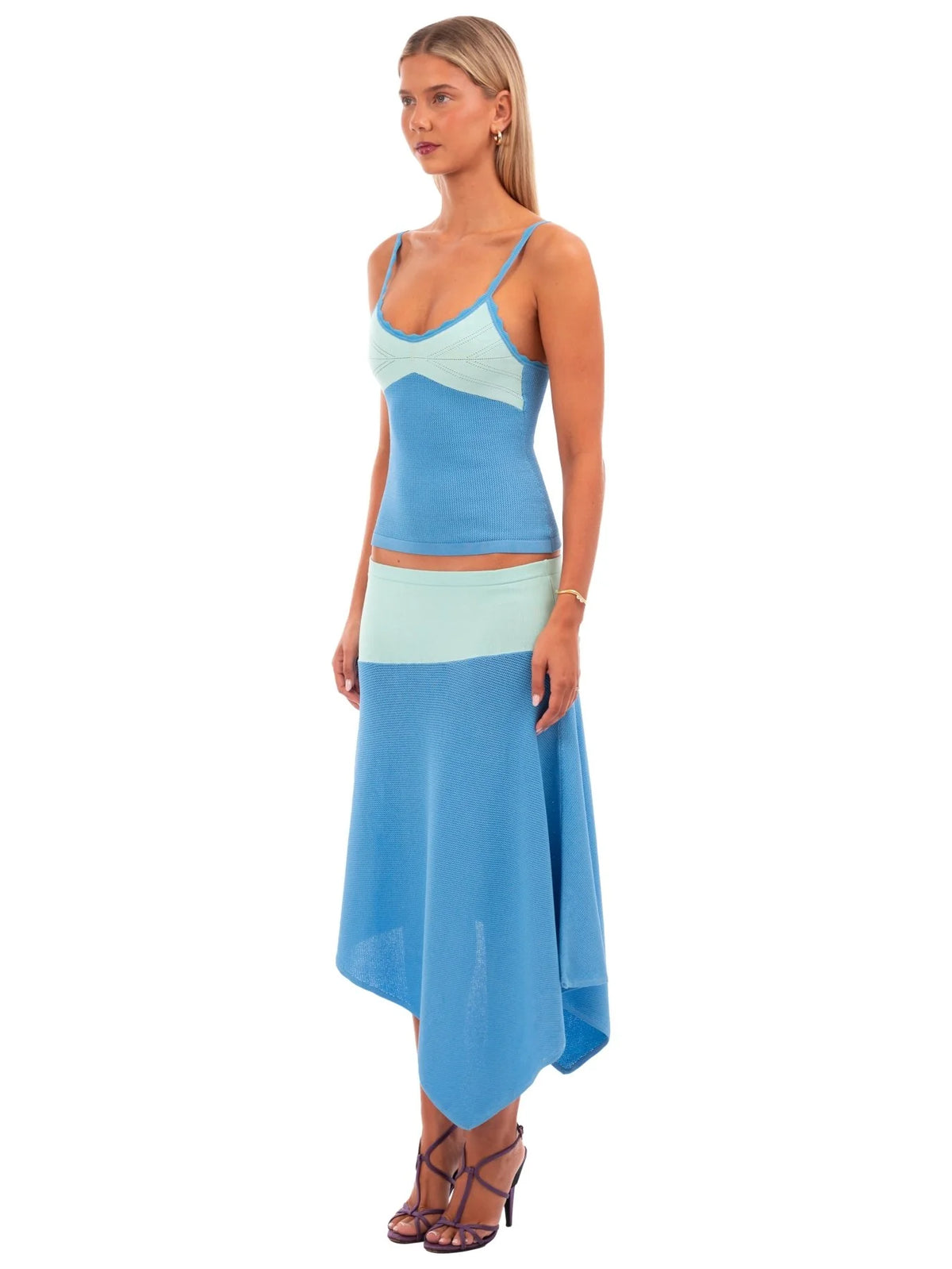 A woman modeling a two-piece color-blocked knit set featuring a light blue and mint green crop top with spaghetti straps and a matching high-low skirt, set against a plain white background.
