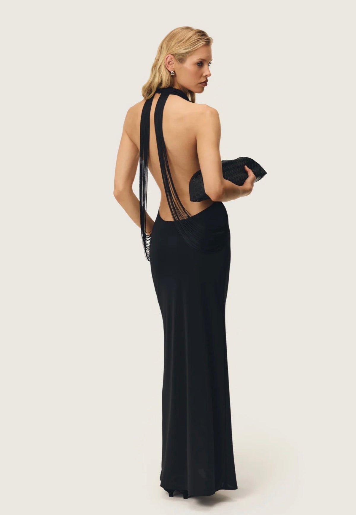 Back view of the Arcina Ori Jean Dress in black, featuring a dramatic open back with long draped tassel detailing and a sleek, floor-length silhouette.