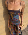 Person wearing a colorful dress with floral patterns against a wooden wall.