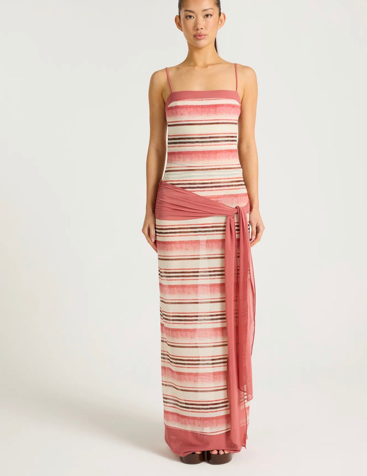 Model wearing the Benni Suki Maxi Dress, featuring a sheer pink, cream and brown striped print with thin straps and a draped pink hip tie.