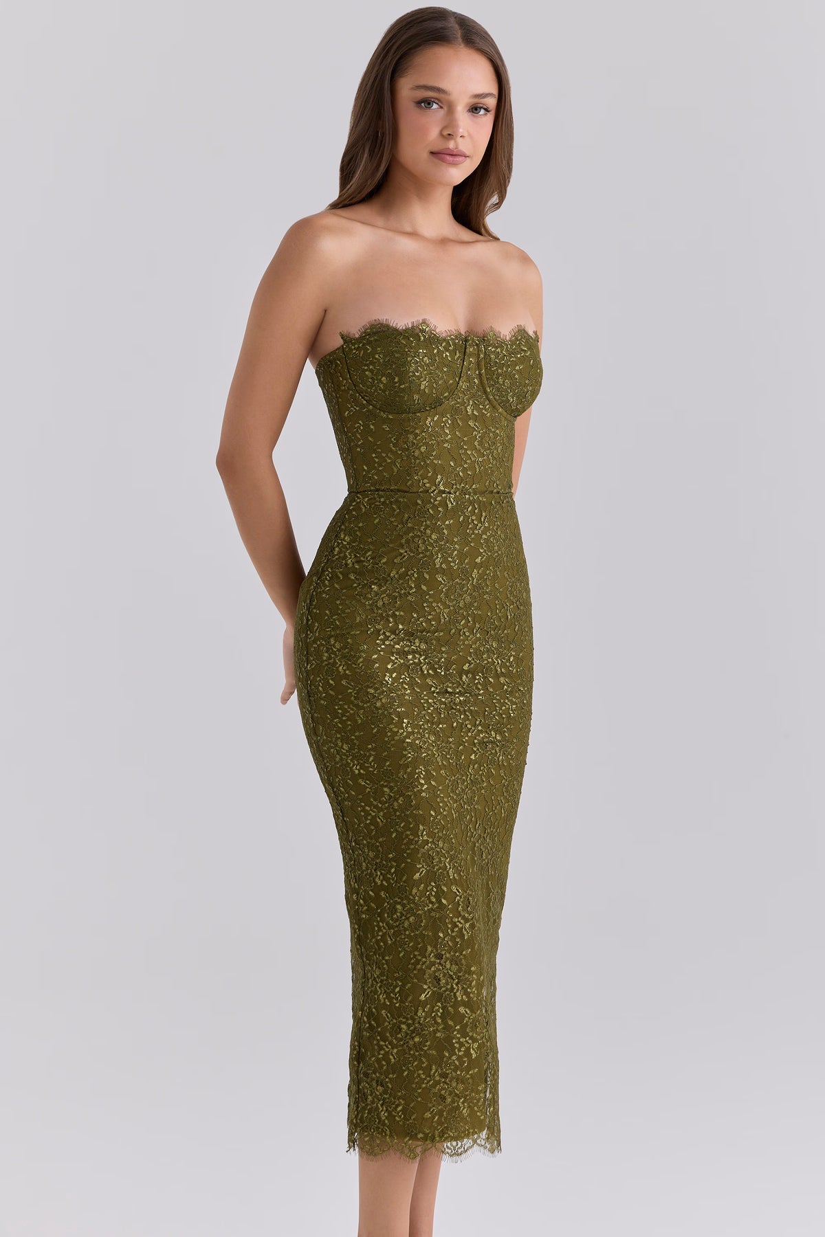 Woman wearing the House of CB Alexia Midi Dress in olive, featuring metallic floral lace, a strapless corset-style bodice and fitted midi silhouette in front of a white backdrop.