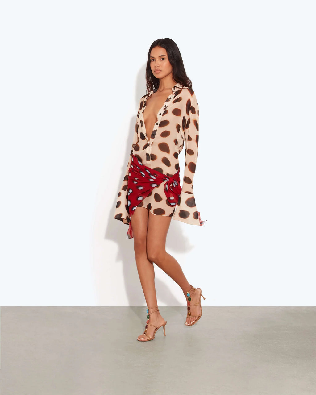 Model wearing the Rat & Boa Nilah Shirt Dress, featuring a sheer cream fabric with bold brown spots, button-down front and long sleeves, styled with a contrasting red printed scarf tied at the waist.