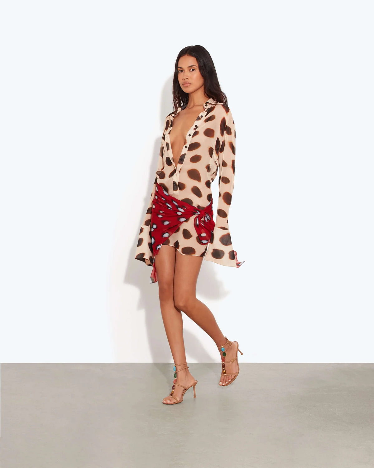 Model wearing the Rat & Boa Nilah Shirt Dress, featuring a sheer cream fabric with bold brown spots, button-down front and long sleeves, styled with a contrasting red printed scarf tied at the waist.