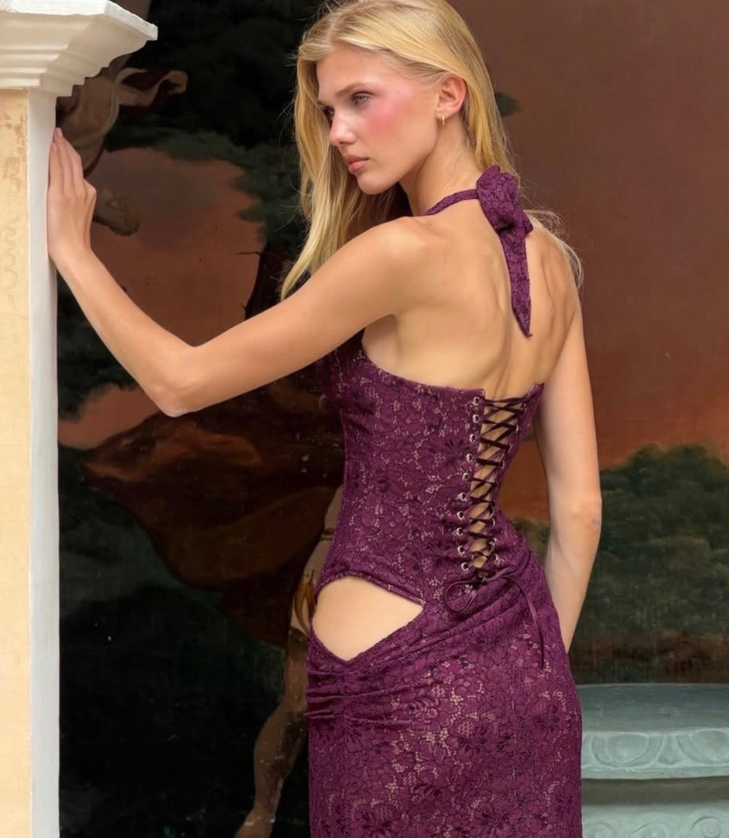 Model wearing the Fenity Veronica Dress in Burgundy, featuring a floral lace corset bodice, halter neckline, plunging lace-trimmed bust, open hip detailing and a fitted draped maxi skirt.