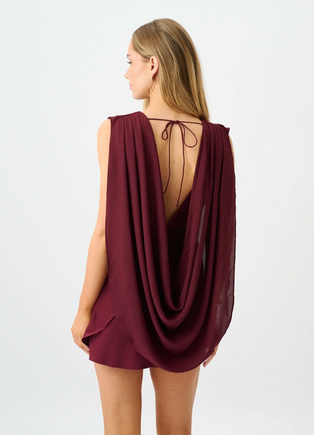 Back view of the With Harper Lu Paige Mini Dress in Burgundy, featuring an open back with delicate tie detailing, a flowing draped georgette cape and a tulip mini skirt.