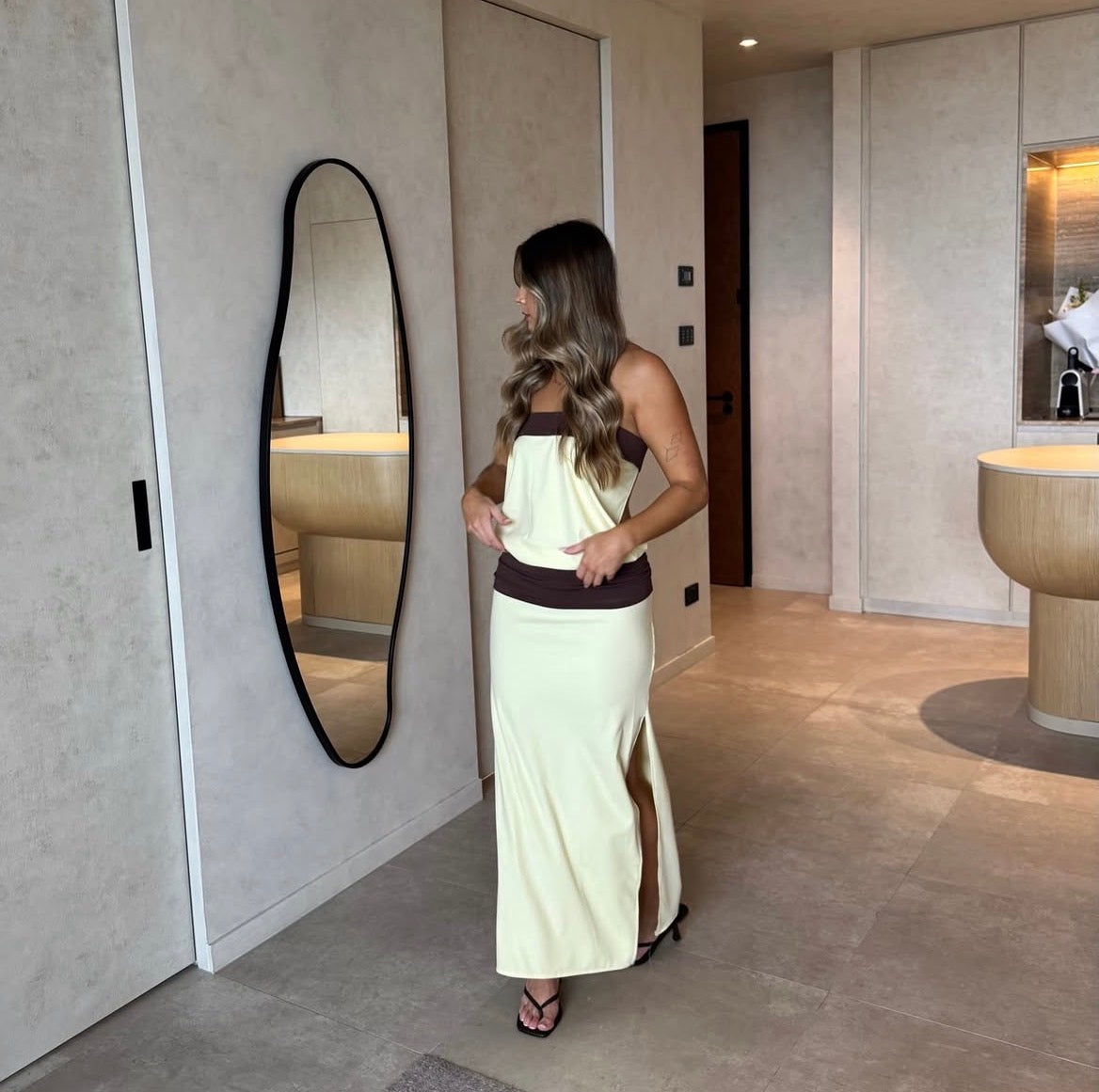 Woman in a long white dress standing in a modern bathroom.