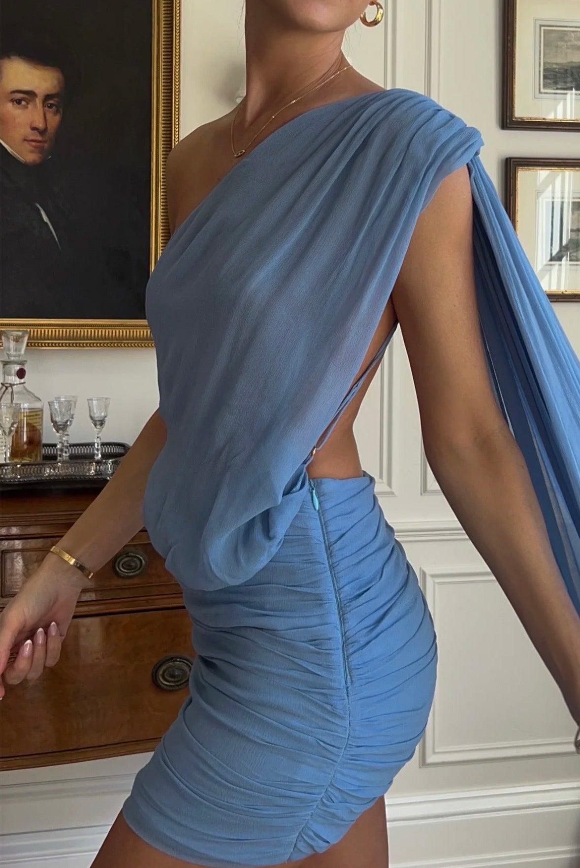 Close-up of the Arcina Ori Fernanda Mini Dress in Blue, featuring a draped one-shoulder neckline, open side detailing, ruched fitted mini skirt and flowing sash.