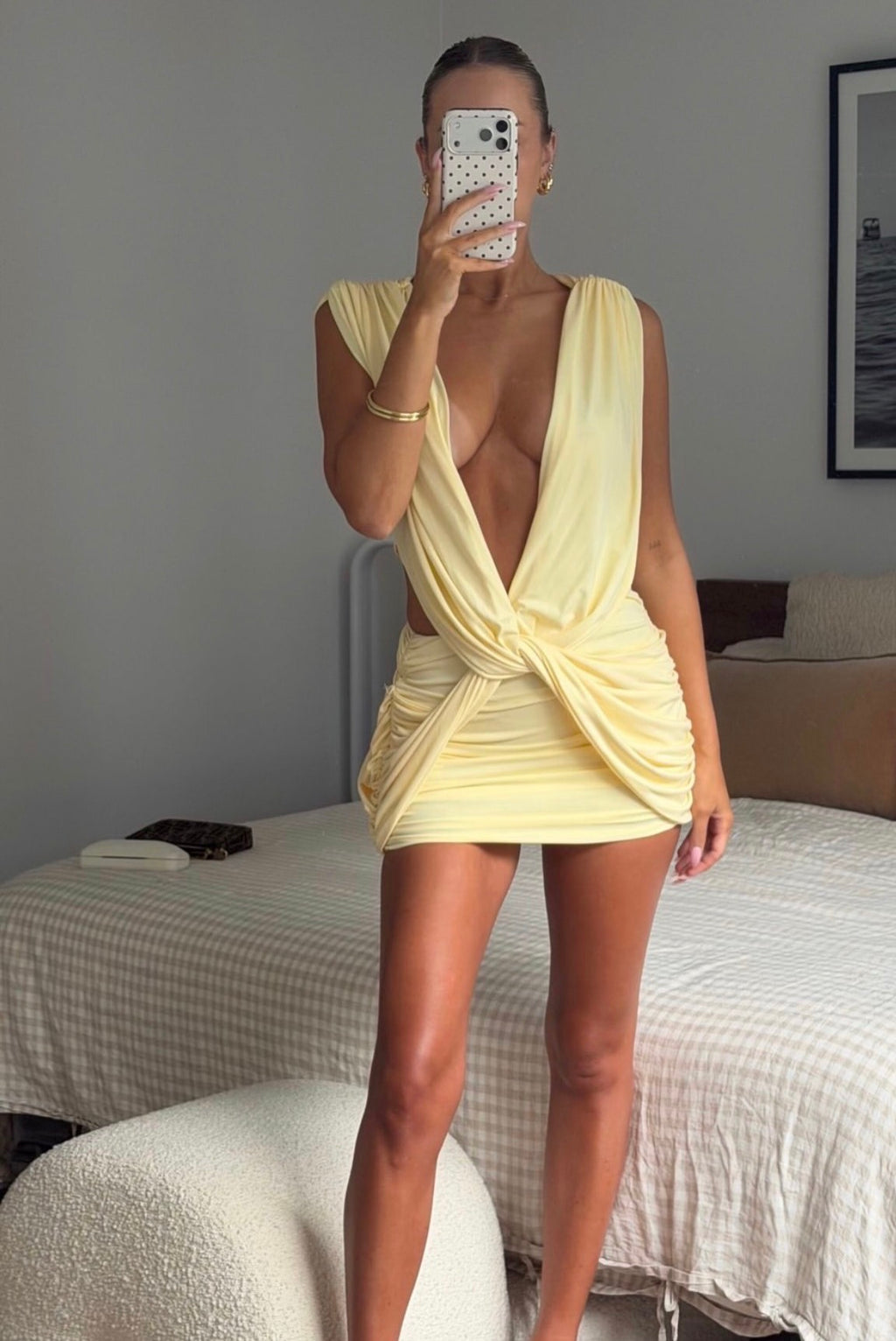 Person wearing a yellow dress taking a mirror selfie in a bedroom.