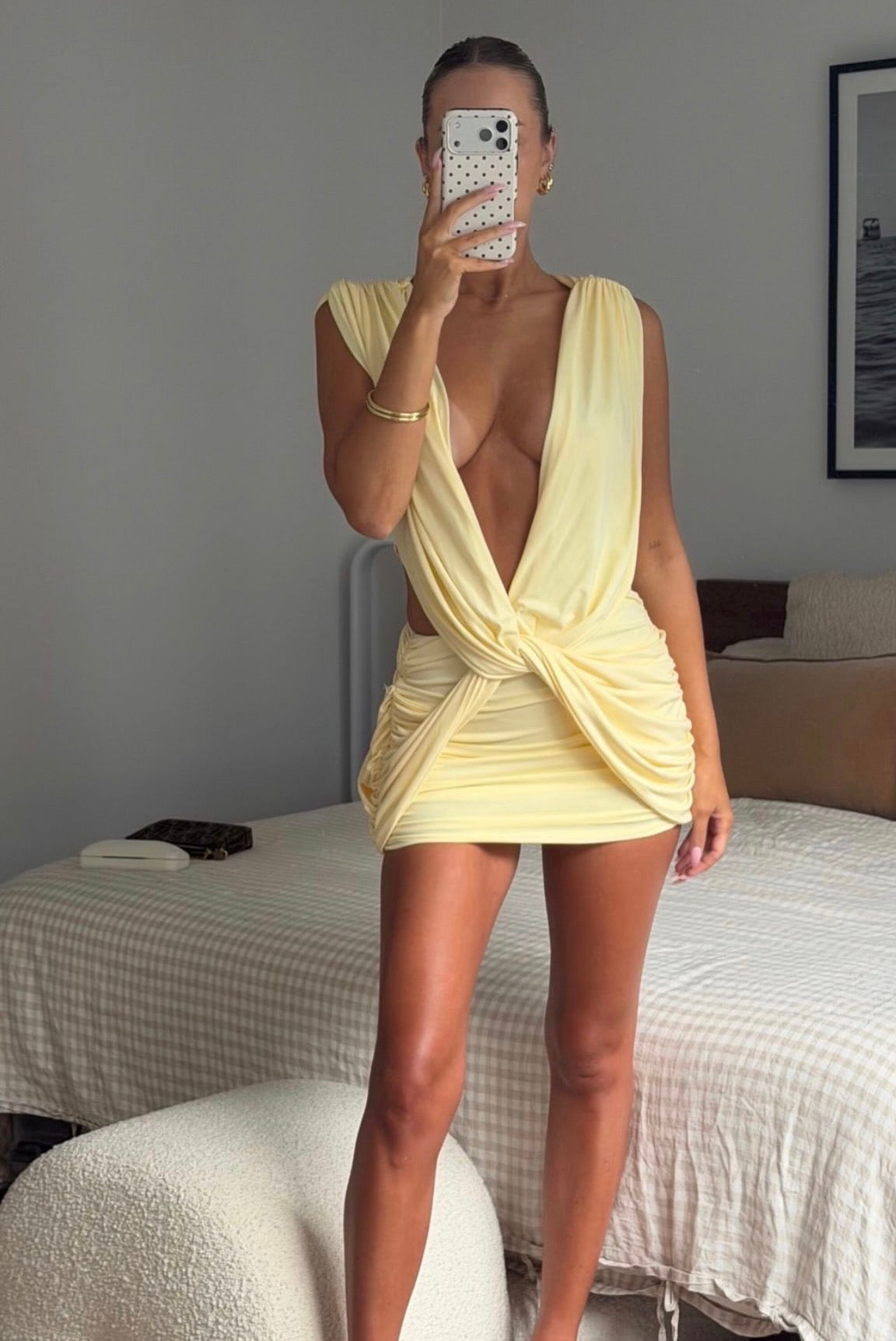 Person wearing a yellow dress taking a mirror selfie in a bedroom.