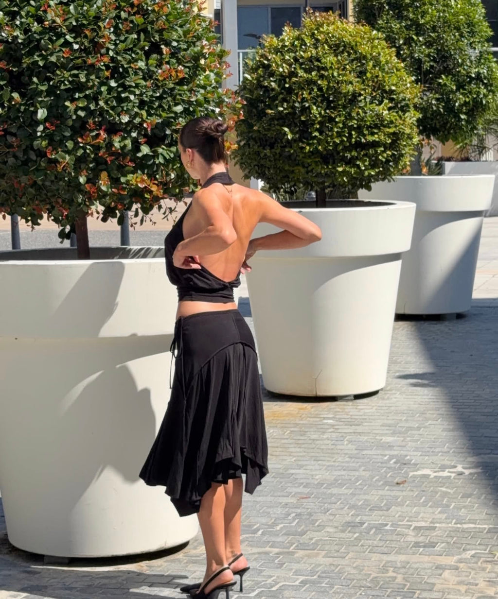 Woman in a black outfit standing next to large white planters with greenery.