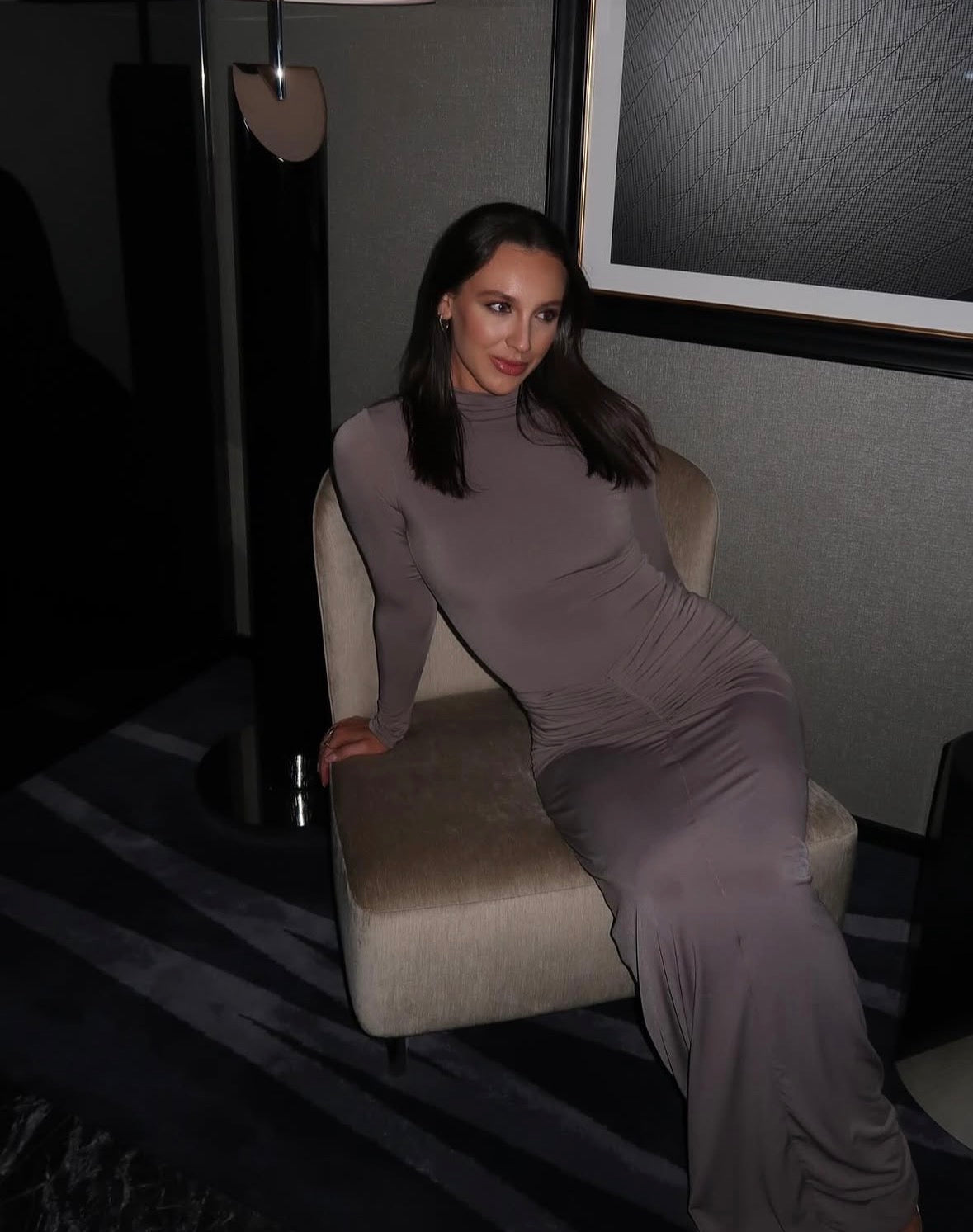 Woman in a long, dark dress sitting on a chair in a dimly lit room.