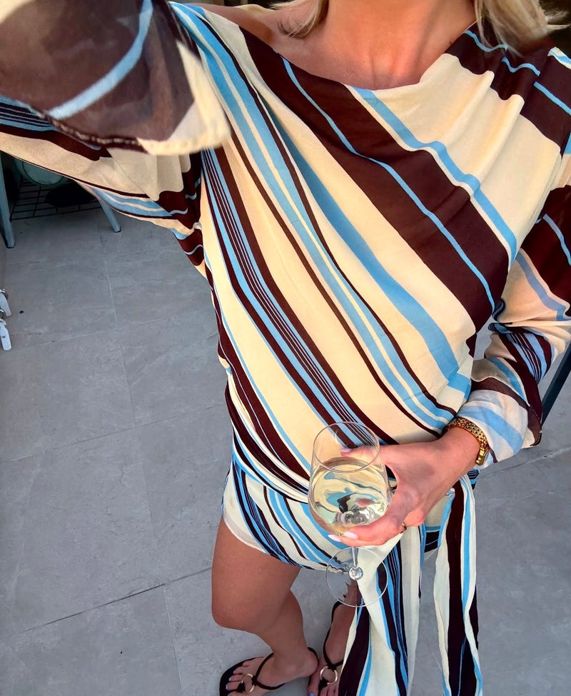 Person wearing a striped dress holding a glass of wine on a tiled floor. - @kaitlynmurray
