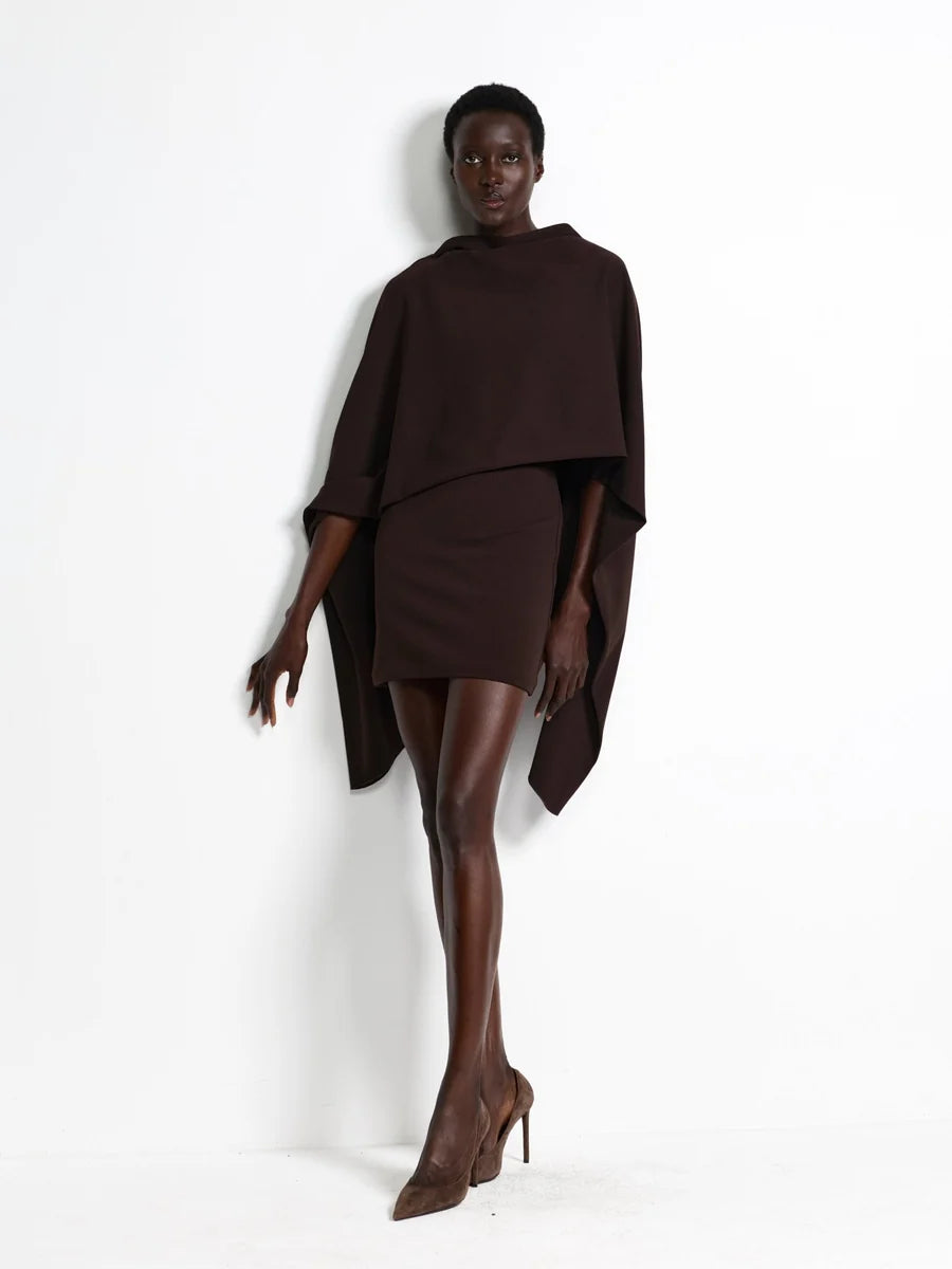 Model wearing the Effie Kats Kathryn Mini Dress in Coffee, featuring a high neckline, structured mini silhouette and oversized draped cape detailing, styled with brown pointed-toe heels against a white studio background.