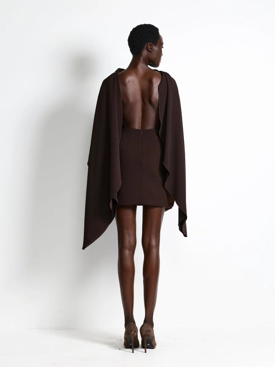 Back view of the Effie Kats Kathryn Mini Dress in Coffee, featuring a dramatic open back, fitted mini skirt and flowing cape-style panels draped from the shoulders, styled with brown heels.