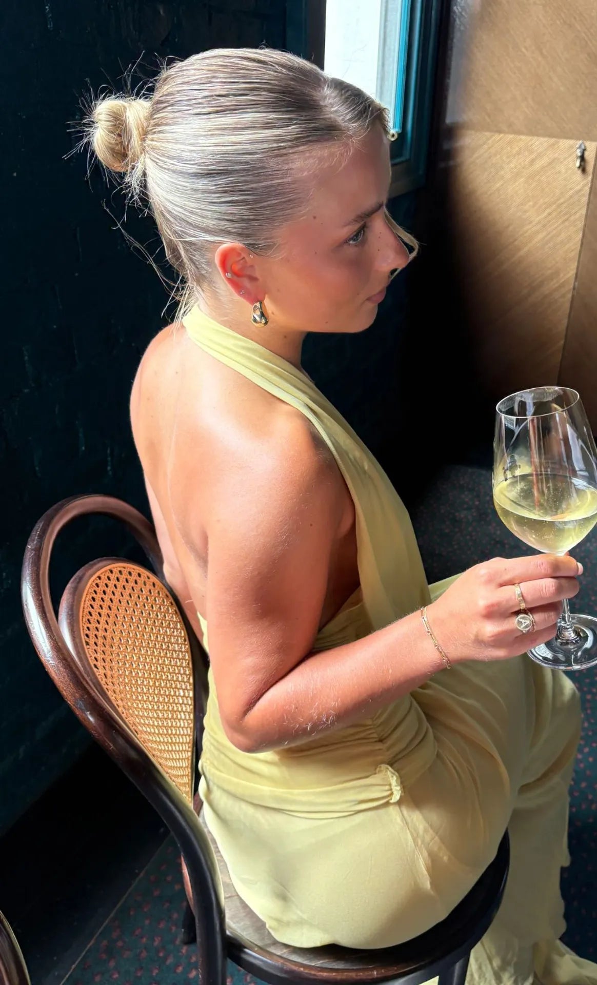 Woman in a yellow dress holding a glass of white wine, sitting on a chair.
