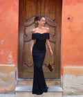 Woman in a black off-shoulder dress standing in front of a wooden door.