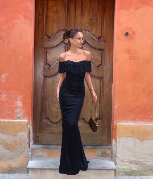 Woman in a black off-shoulder dress standing in front of a wooden door.