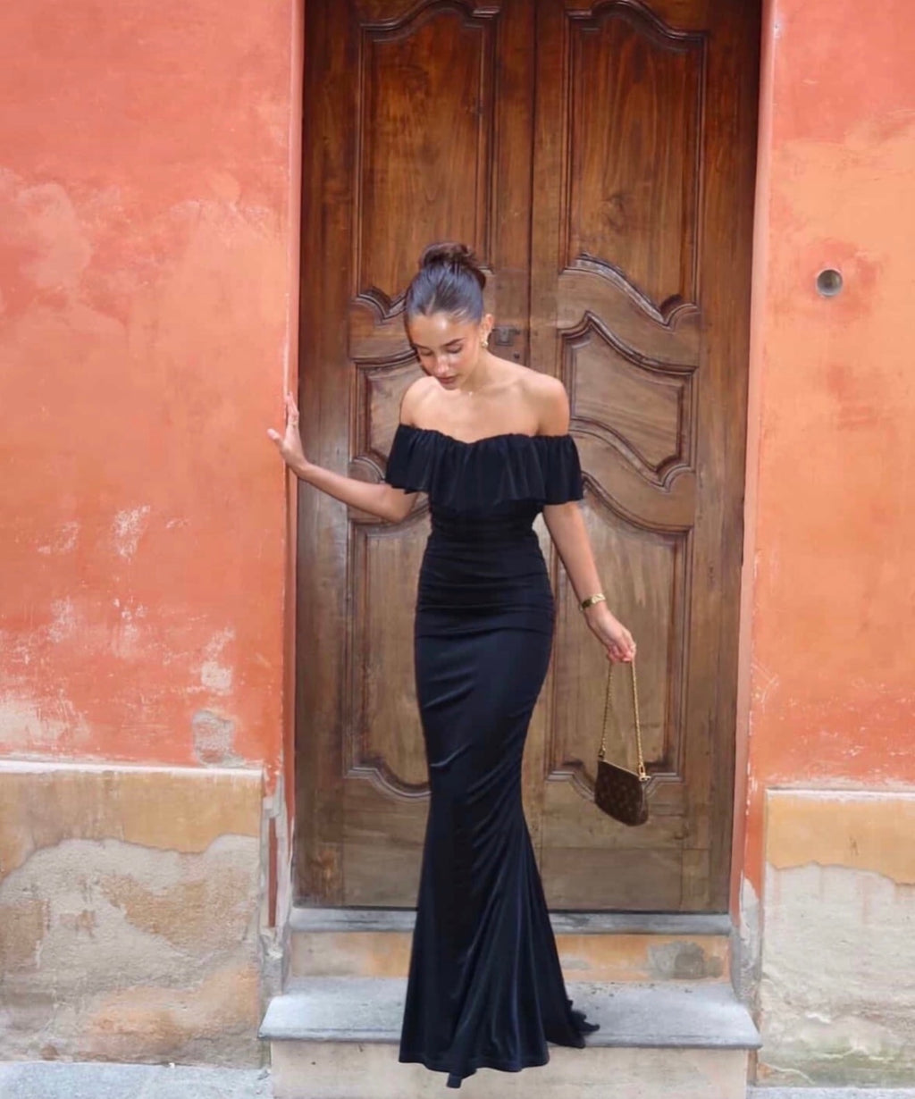 Woman in a black off-shoulder dress standing in front of a wooden door on a colorful wall.