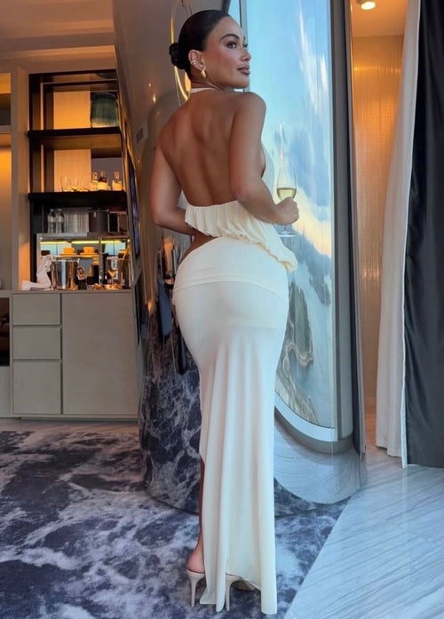 Woman in a white evening gown standing by a large window with a cityscape view.