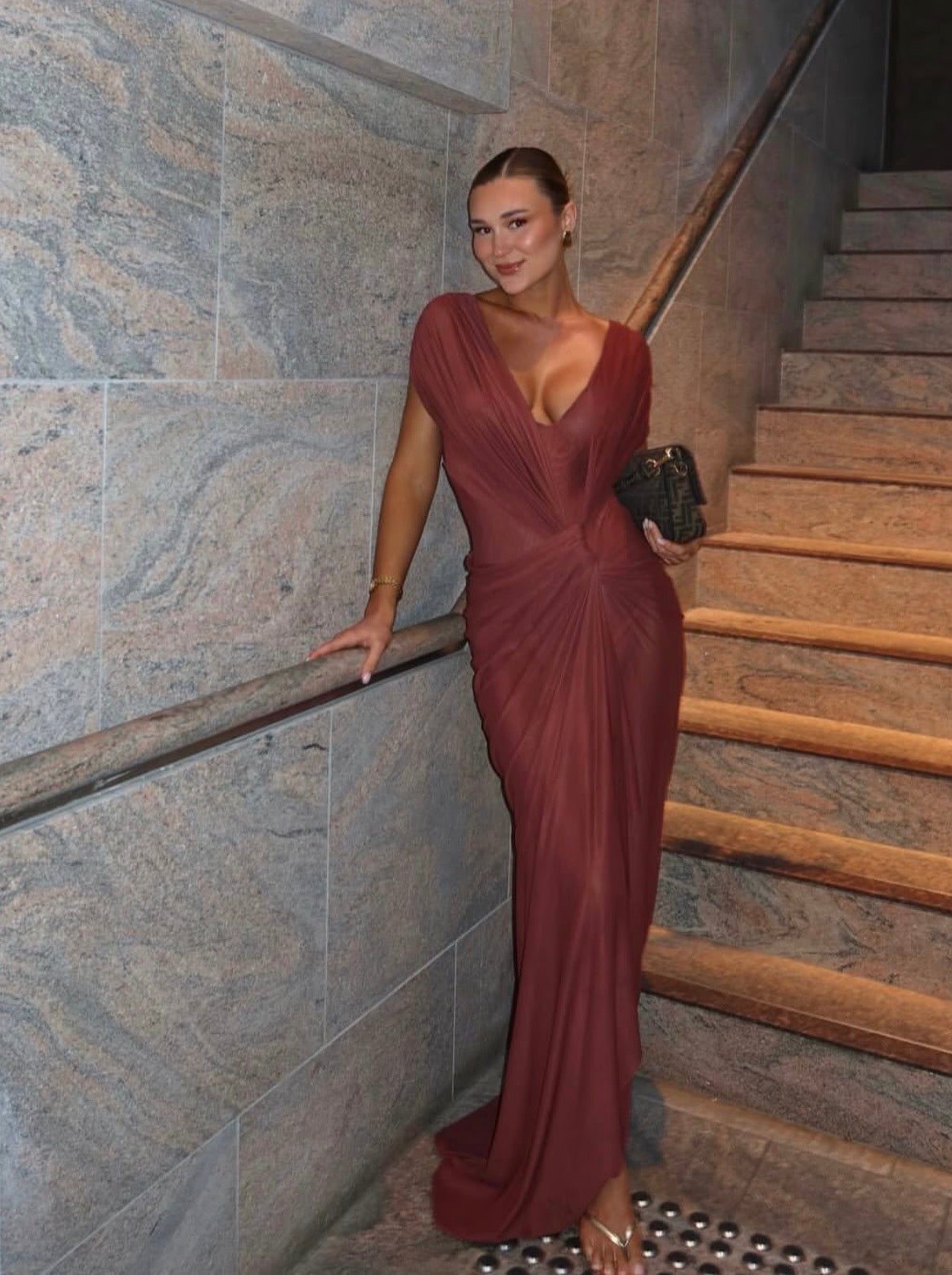Woman in a burgundy evening gown standing on a staircase with stone walls. -  @shanigrimmond
