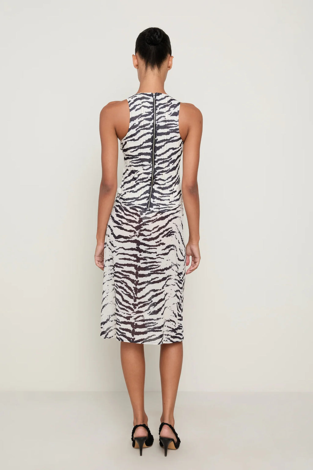 Back view of a model wearing the Miaou Annika Corset and Aimeé Skirt matching set in black and white zebra print, featuring a fitted sleeveless corset with a full-length back zipper and a coordinating sheer midi skirt with a subtly flared hem, styled with black heels against a neutral studio background.
