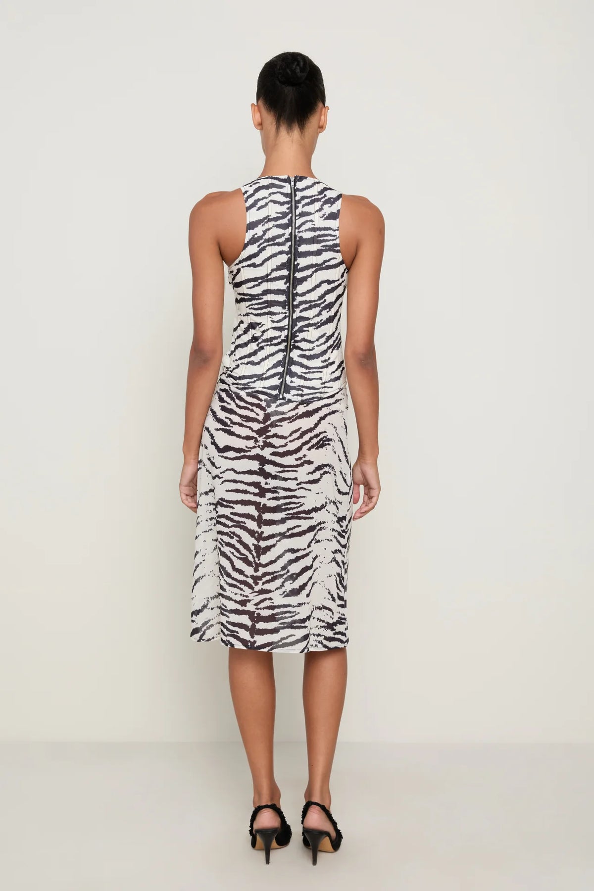 Back view of a model wearing the Miaou Annika Corset and Aimeé Skirt matching set in black and white zebra print, featuring a fitted sleeveless corset with a full-length back zipper and a coordinating sheer midi skirt with a subtly flared hem, styled with black heels against a neutral studio background.
