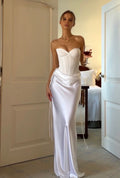 Woman in a white strapless gown standing in a room with a table and chairs.
