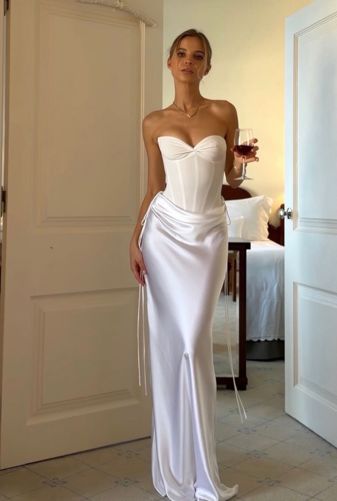 Woman in a white strapless gown standing in a room with a table and chairs.