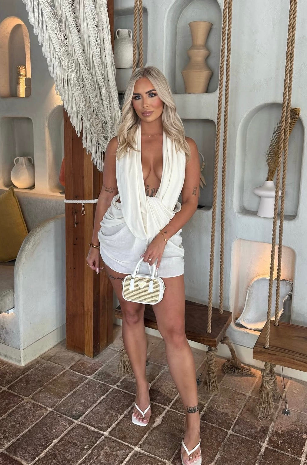 Woman in a white dress standing in a stylish interior setting with decorative elements.