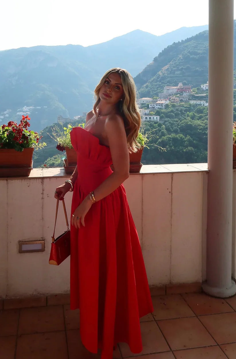 Woman in a red dress standing on a balcony with scenic mountains in the background