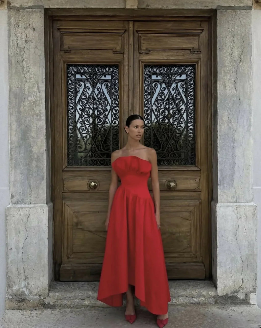 Woman in a red dress standing in front of a wooden door with intricate designs.