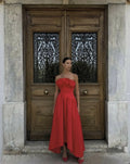 Woman in a red dress standing in front of a wooden door with intricate designs.