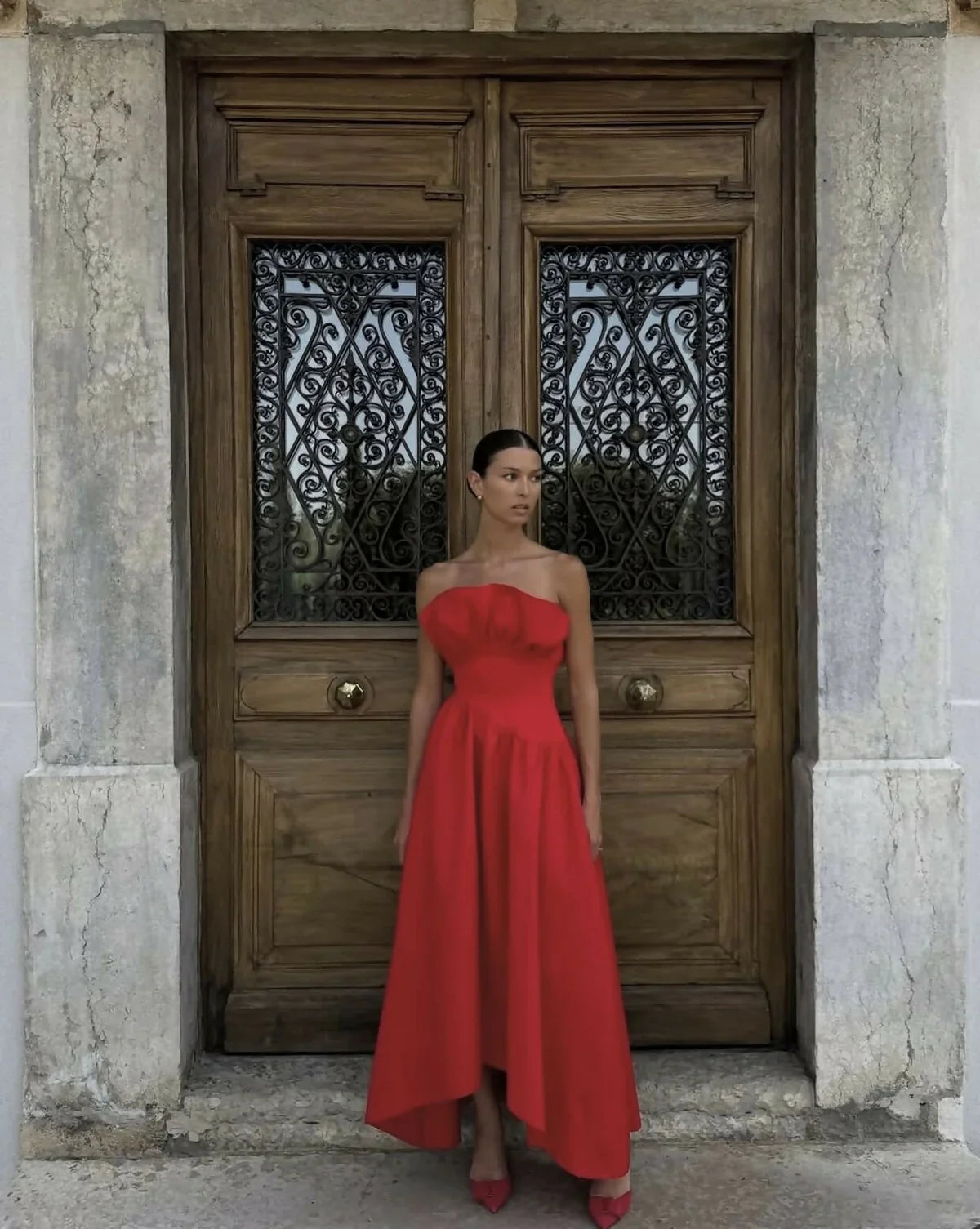 Woman in a red dress standing in front of a wooden door with intricate designs.