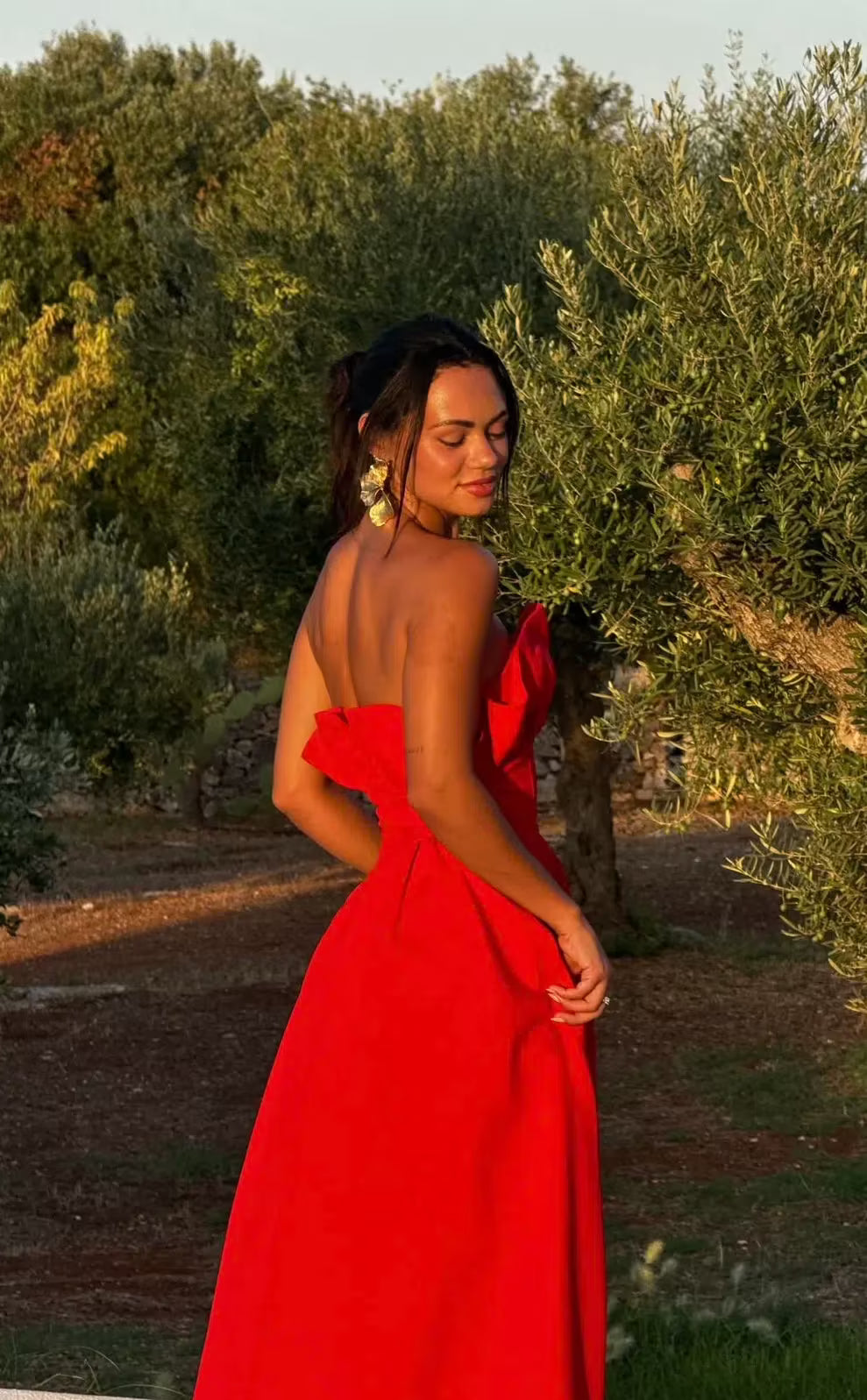 Woman in a red dress standing in an outdoor setting with greenery.