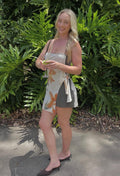 Woman standing outdoors with green foliage in the background. - @elliekate__